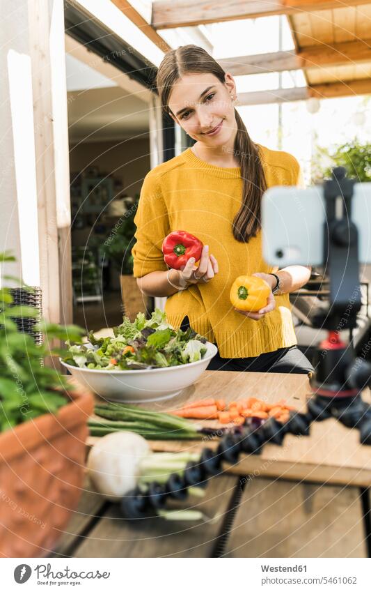 Lächelnde Frau filmt mit dem Handy, während sie zu Hause Essen zubereitet Farbaufnahme Farbe Farbfoto Farbphoto Deutschland Freizeitkleidung Freizeitbekleidung