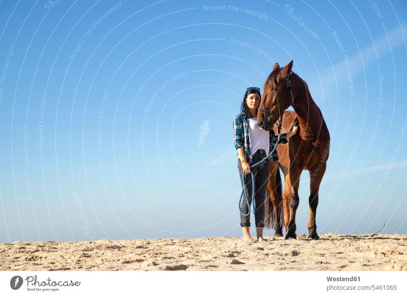 Frau mit Pferd stehend im Sand steht weiblich Frauen Equus caballus Pferde sandig Erwachsener erwachsen Mensch Menschen Leute People Personen Säugetier Mammalia