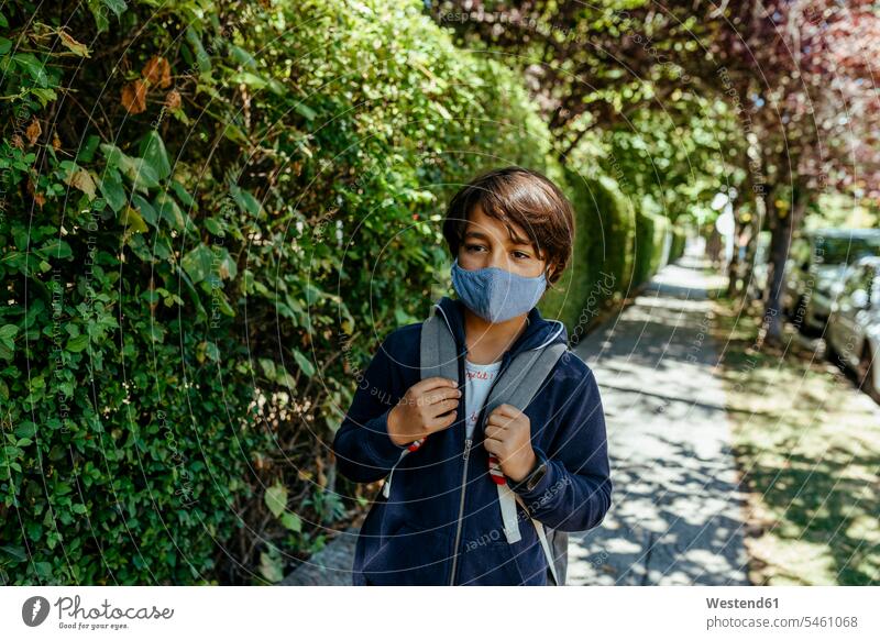 Schuljunge mit Maske schaut weg, während er an Pflanzen auf dem Fußweg steht Farbaufnahme Farbe Farbfoto Farbphoto Spanien Freizeitkleidung Freizeitbekleidung