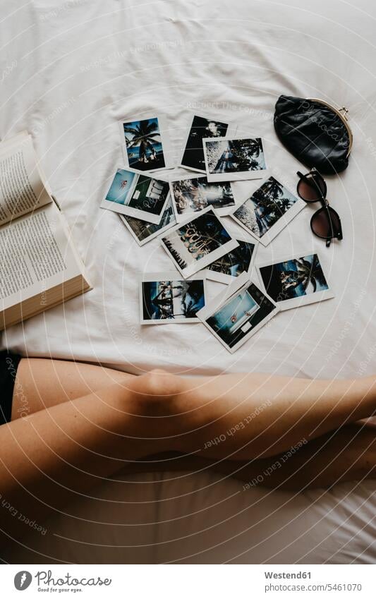 Beine einer jungen Frau im Bett mit Buch und Polaroidbildern Portemonnaies Portmonees Geldboerse Geldboersen Börsen Geldbörsen Erinnerung erinnern Komfort