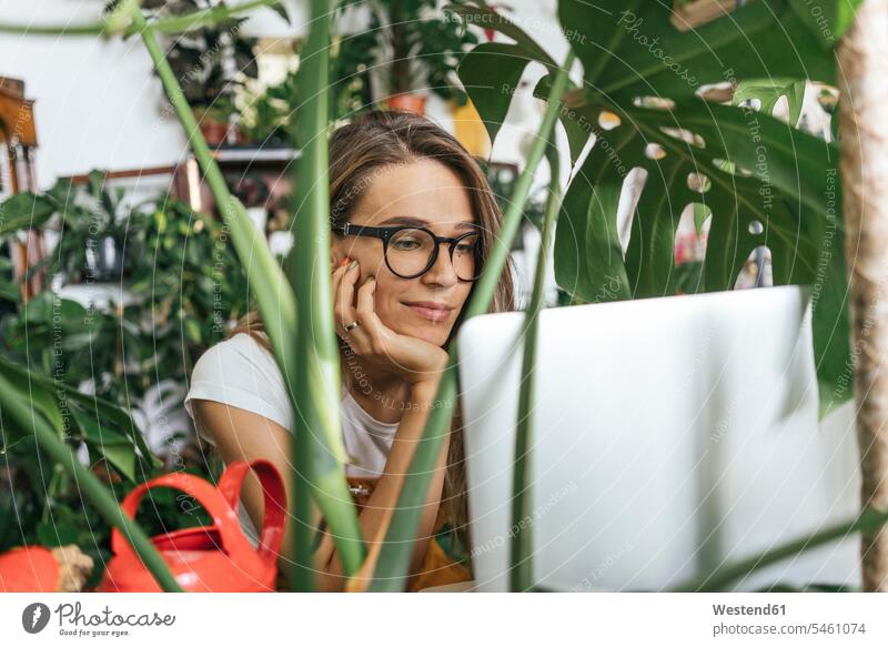 Junge Frau benutzt Laptop inmitten von Pflanzen Job Berufe Berufstätigkeit Beschäftigung Jobs Rechner Laptops Notebook Notebooks Brillen Arbeit leidenschaftlich