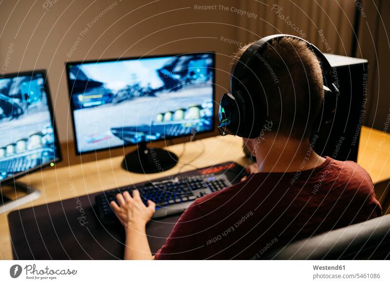 Junger Mann spielt Videospiele mit Computer am Schreibtisch Farbaufnahme Farbe Farbfoto Farbphoto Innenaufnahme Innenaufnahmen innen drinnen Computer benutzen