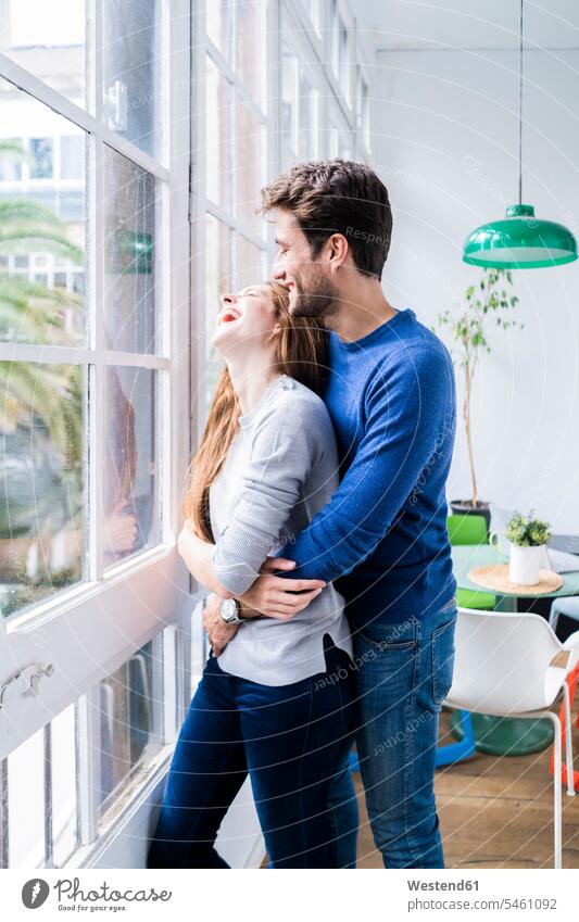 Glücklich zärtliches Paar umarmt am Fenster zu Hause entspannen relaxen knuddeln schmusen Arm umlegen Umarmung Umarmungen entspanntheit relaxt freuen Frohsinn