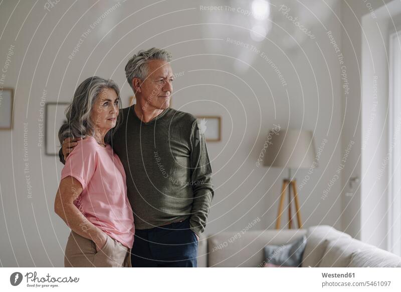 Älteres Ehepaar steht zu Hause im Wohnzimmer Rahmen Bilder Bildnis entspannen relaxen Arm umlegen Umarmung Umarmungen entspanntheit relaxt gefühlvoll Emotionen