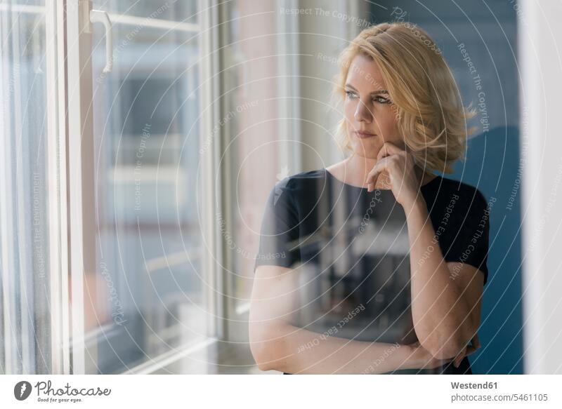 Ernste blonde Frau schaut aus dem Fenster ernst Ernsthaftigkeit ernsthaft weiblich Frauen schauen sehend blonde Haare blondes Haar Erwachsener erwachsen Mensch