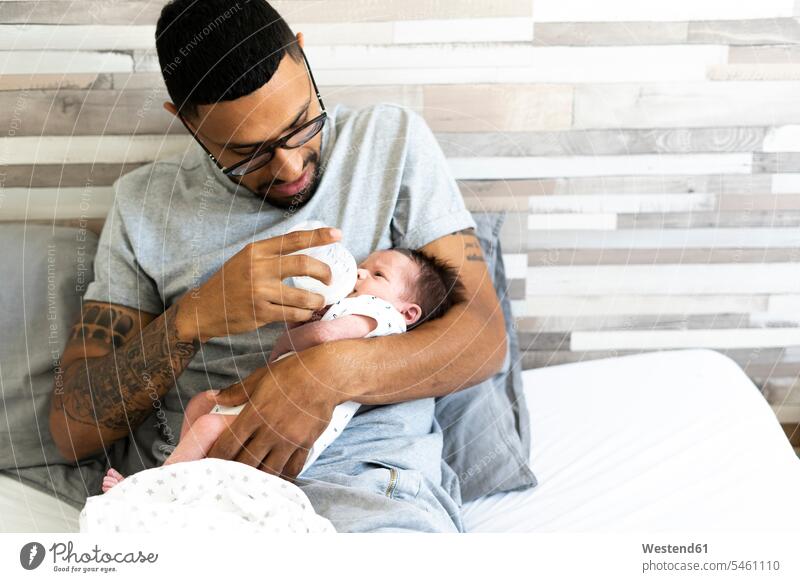 Vater füttert sein neugeborenes Baby im Bett mit der Flasche multikulturell Betten behüten Babies Babys Säuglinge Kind Kinder Babyflasche Babyflaschen