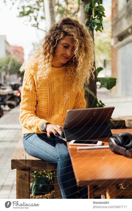 Hübsche blonde Studentin benutzt digitales Tablet, während sie in einem Straßencafé in der Stadt sitzt Farbaufnahme Farbe Farbfoto Farbphoto Spanien