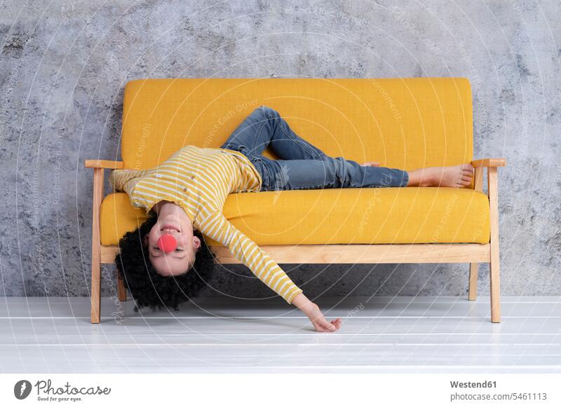 Junge mit roter Clownsnase und schwarzen Haaren auf gelber Couch Couches Liege Sofas entspannen relaxen entspanntheit relaxt freuen Glück glücklich sein