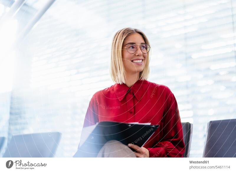 Lächelnde junge Geschäftsfrau mit Mappe sitzt im Wartebereich Job Berufe Berufstätigkeit Beschäftigung Jobs geschäftlich Geschäftsleben Geschäftswelt