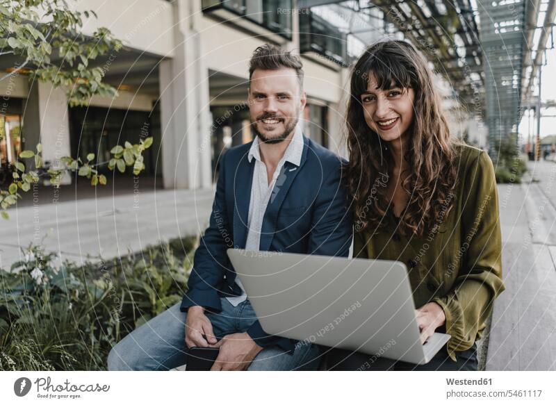 Porträt eines lächelnden Geschäftsmannes und einer lässigen Geschäftsfrau, die einen Laptop im Freien benutzen Leute Menschen People Person Personen Europäisch