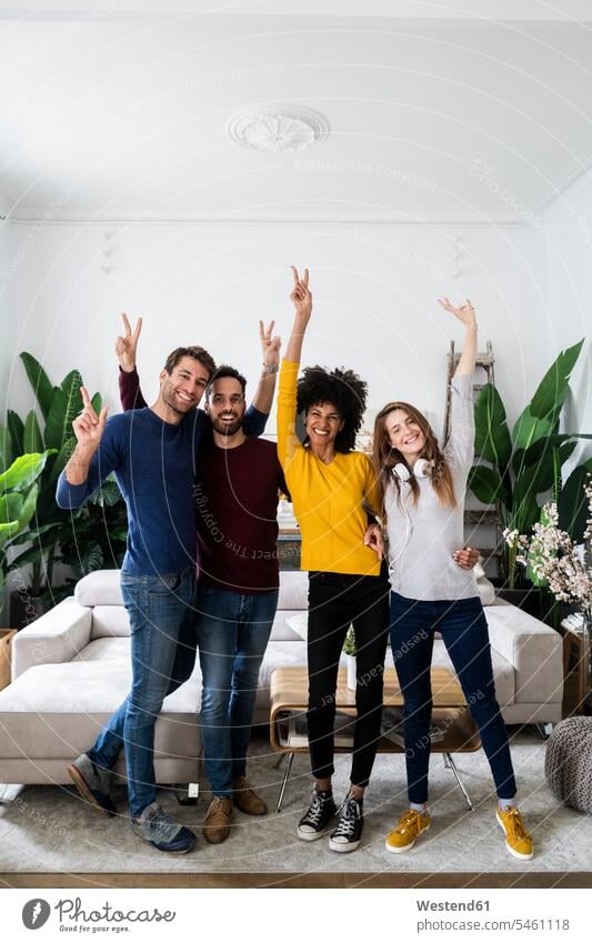 Porträt von vier glücklichen Freunden, die Seite an Seite im Wohnzimmer stehen Kameradschaft Couch Couches Liege Sofas Kopfhoerer freuen Frohsinn Fröhlichkeit