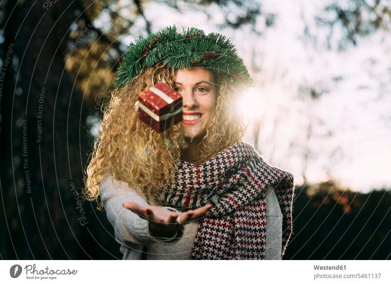 Porträt einer lächelnden jungen Frau mit Weihnachtskranz auf dem Kopf, die mit einem Weihnachtsgeschenk jongliert Schals abends freuen Frohsinn Fröhlichkeit