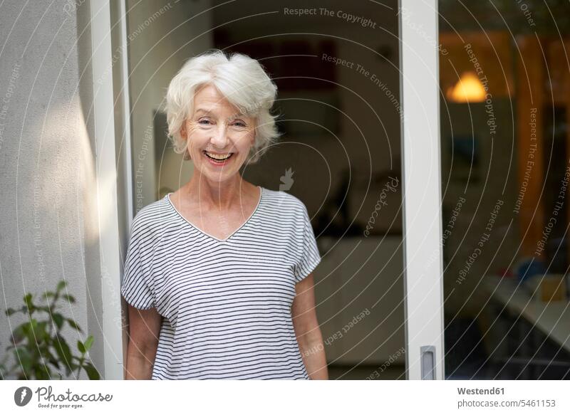 Porträt einer lachenden, reifen Frau, die abends vor einer geöffneten Terrassentür steht T-Shirts freuen Glück glücklich sein glücklichsein zufrieden stehend
