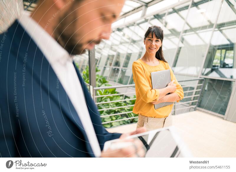 Lächelnde weibliche Unternehmerin, die einen männlichen Kollegen bei der Verwendung eines digitalen Tablets im Büro betrachtet Farbaufnahme Farbe Farbfoto