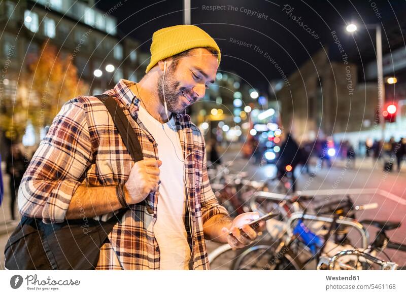 UK, London, Mann pendelt nachts in der Stadt und schaut auf sein Telefon Männer männlich pendeln Handy Mobiltelefon Handies Handys Mobiltelefone ansehen Nacht