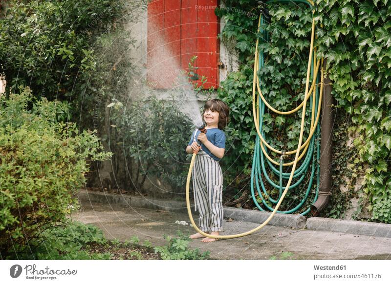 Junge genießt Gartenschlauch in der Hand, während er Pflanzen im Garten gießt ländliches Motiv nicht städtisch Farbaufnahme Farbe Farbfoto Farbphoto