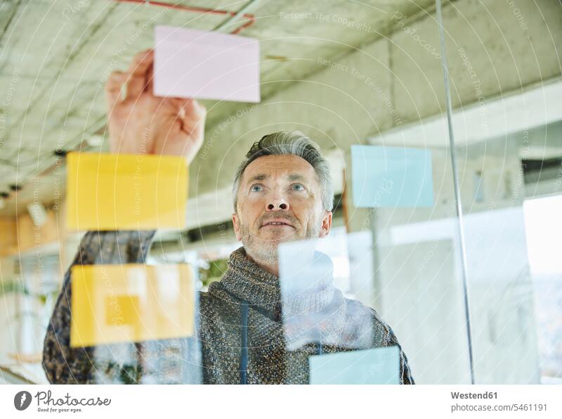 Männlich reifen Geschäftsmann Putting Note auf Glaswand während der Arbeit im Büro Farbaufnahme Farbe Farbfoto Farbphoto Innenaufnahme Innenaufnahmen innen
