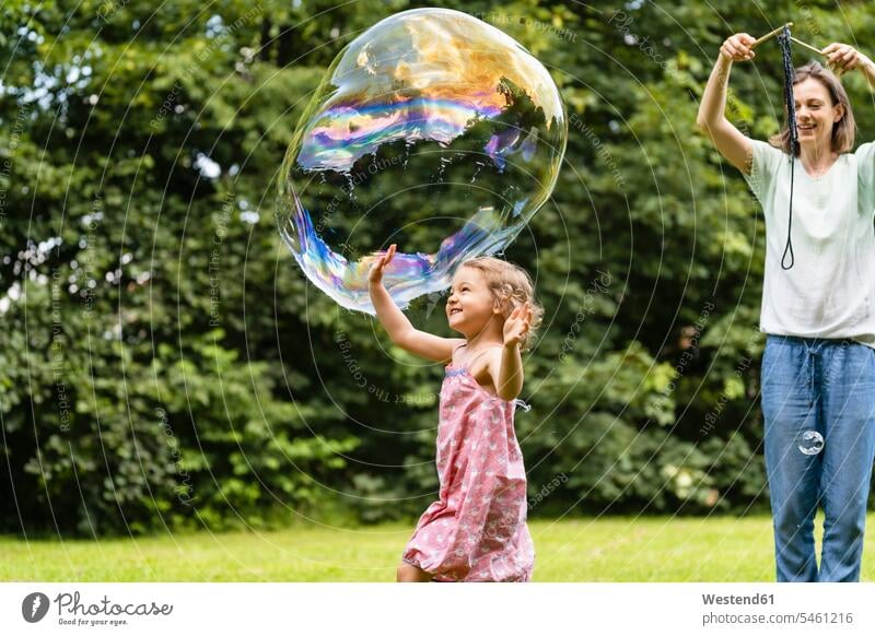 Mutter und Tochter spielen mit Blase im Park Farbaufnahme Farbe Farbfoto Farbphoto Außenaufnahme außen draußen im Freien Tag Tageslichtaufnahme