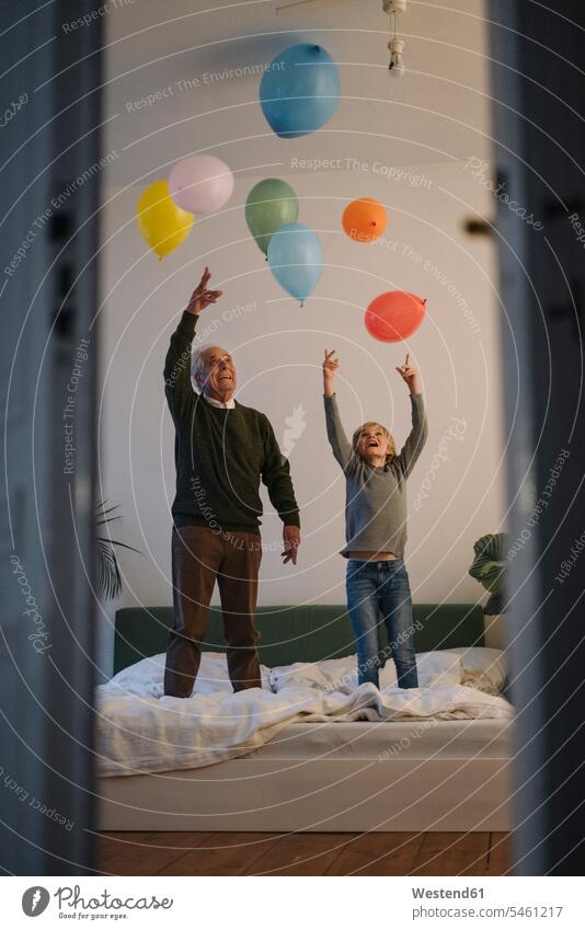 Glücklicher Grossvater und Enkel spielen zu Hause mit Luftballons auf dem Bett Leute Menschen People Person Personen Europäisch Kaukasier kaukasisch 2