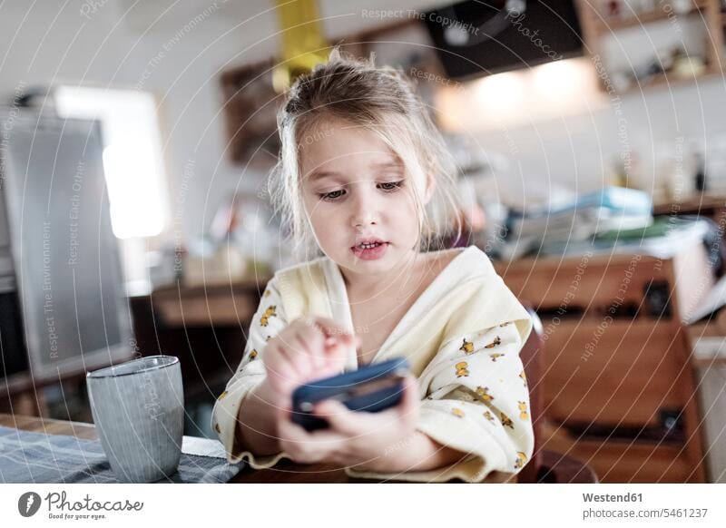 Porträt des kleinen Mädchens sitzt am Frühstückstisch in der Küche mit Smartphone benutzen benützen sitzen sitzend Küchen weiblich Frühstückstische