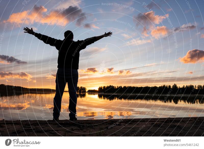 Finnland, Kajaani, Mann beobachtet Sonnenuntergang am Fluss mit ausgestreckten Armen Abend abends reisen Travel verreisen Weg Reise Unabhängigkeit selbständig