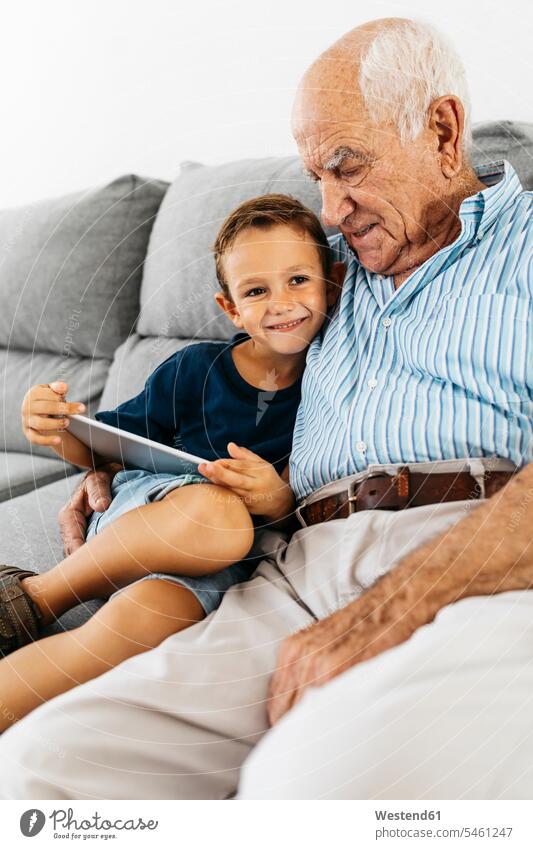 Porträt von glücklichen kleinen Jungen mit digitalen Tablette sitzt neben seinem Großvater auf der Couch zu Hause Portrait Porträts Portraits Glück