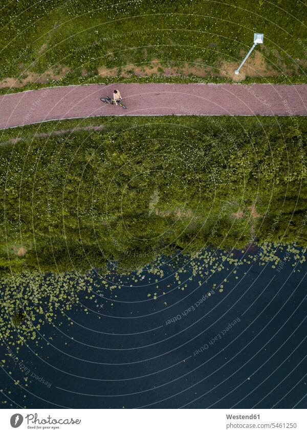 Russland, Tichwin, Luftaufnahme einer Radfahrerin bei einer Pause auf einem Seeufer-Wanderweg im Park Außenaufnahme außen draußen im Freien Tag