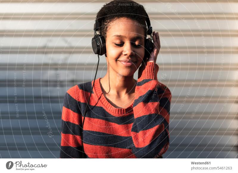 Porträt einer lächelnden jungen Frau, die mit Kopfhörern Musik hört weiblich Frauen Portrait Porträts Portraits hören hoeren Erwachsener erwachsen Mensch