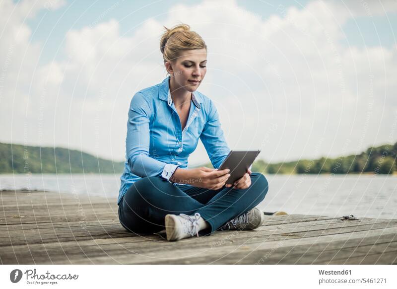 Frau sitzt auf Steg an einem See mit Tablet Stege Anlegestelle Seen Tablet Computer Tablet-PC Tablet PC iPad Tablet-Computer weiblich Frauen sitzen sitzend