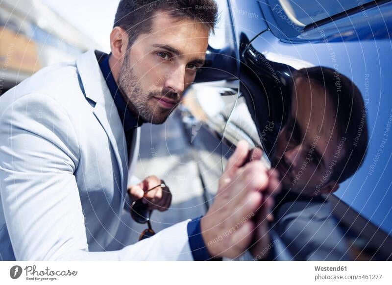 Junger Geschäftsmann streichelt sein poliertes Auto Businessmann Businessmänner Geschäftsmänner Wagen PKWs Automobil Autos unterwegs auf Achse in Bewegung
