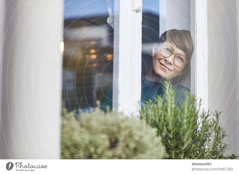 Lächelnde Frau zu Hause, die aus dem Fenster schaut Leute Menschen People Person Personen Alleinstehende Alleinstehender Singles Unverheiratete Unverheirateter