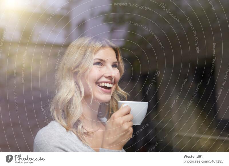 Porträt einer lachenden Frau mit einer Tasse Kaffee hinter einer Fensterscheibe Kaffeetasse Kaffeetassen Portrait Porträts Portraits weiblich Frauen
