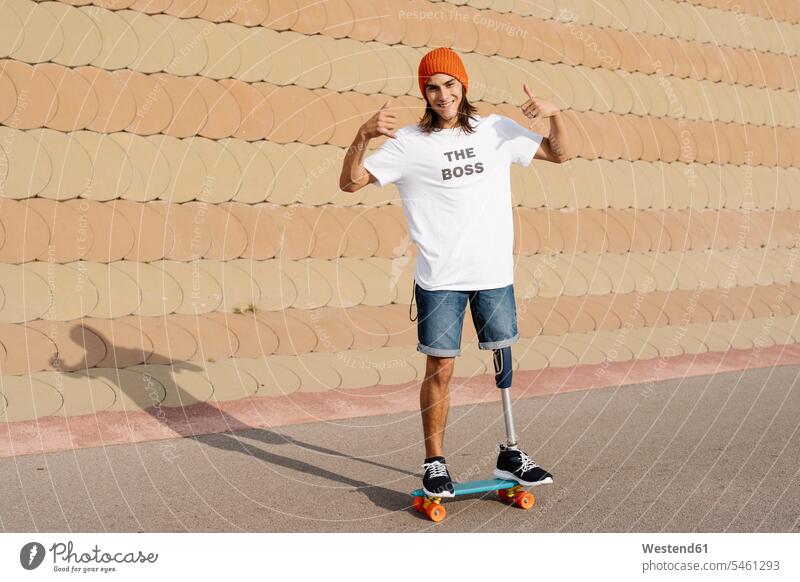 Junger behinderter Mann steht auf Skateboard am Sportplatz Farbaufnahme Farbe Farbfoto Farbphoto Außenaufnahme außen draußen im Freien Tag Tageslichtaufnahme