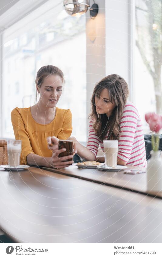 Zwei Freundinnen treffen sich mit einem Smartphone in einem Café Treffen Begegnung iPhone Smartphones benutzen benützen Cafe Kaffeehaus Bistro Cafes
