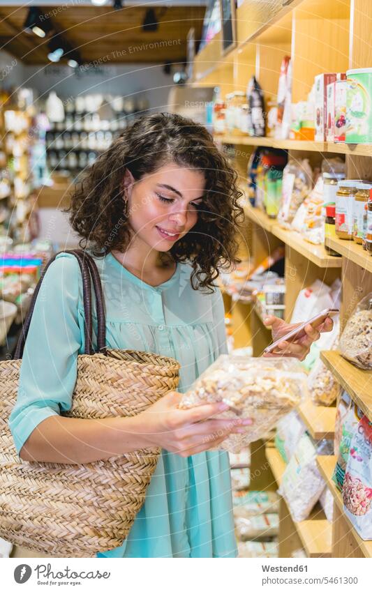 Junge Frau beim Einkaufen in einem Lebensmittelgeschäft Taschen Einkaufstaschen Ablage Regale Telekommunikation telefonieren Handies Handys Mobiltelefon
