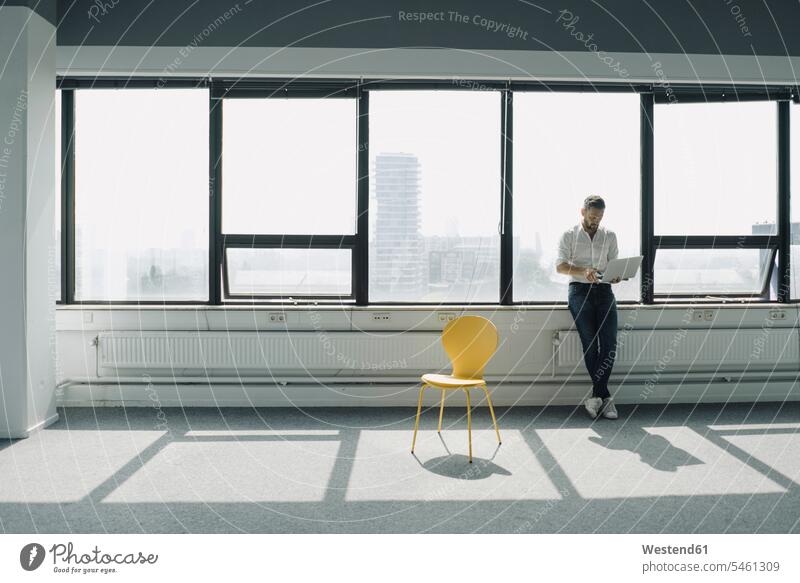 Reifer Geschäftsmann mit Laptop am Fenster im leeren Büro Job Berufe Berufstätigkeit Beschäftigung Jobs geschäftlich Geschäftsleben Geschäftswelt