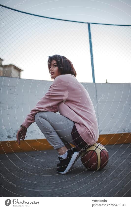 Junge Frau sitzt auf Basketball im Freien weiblich Frauen Zaun Zäune Basketbaelle Basketbälle Erwachsener erwachsen Mensch Menschen Leute People Personen Sport