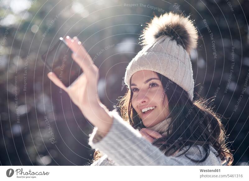 Porträt einer lächelnden jungen Frau, die ein Selfie mit ihrem Smartphone im Winterwald macht Selfies weiblich Frauen iPhone Smartphones Portrait Porträts