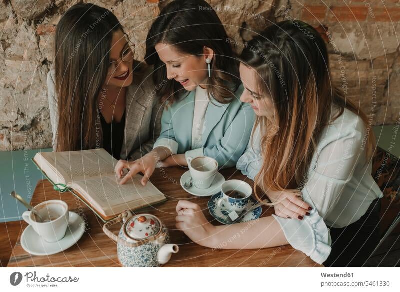 Drei junge Frauen lesen ein Buch in einem Café Spanien modisch rustikal Mauerwerk Gemeinsamkeit zusammen gemeinsam Teilen Sharing Teetasse Teetassen Intelligenz