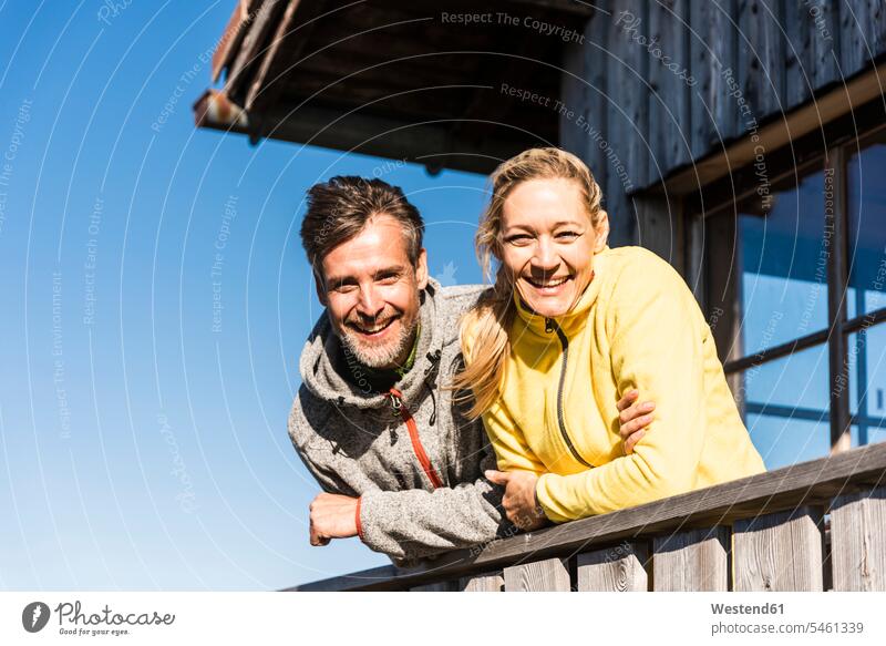 Paar lehnt auf Balkon einer Berghütte, lächelnd bergsteigen Bergsteiger aufstützen aufgestuetzt aufgestützt Pärchen Paare Partnerschaft Alm Alp Bergweide Almen