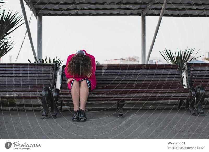 Depressive Frau mit lockigem Haar sitzt auf einer Bank Locken lockiges Haar gelockte Haare gelocktes Haar Depression depressiv Sitzbänke Bänke Sitzbank sitzen