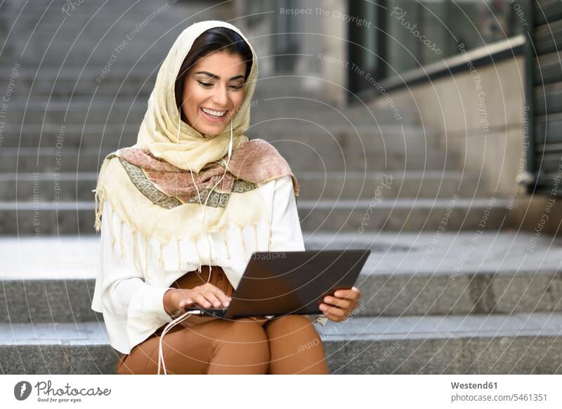 Spanien, Granada, junge muslimische Frau trägt Hijab mit Laptop sitzen auf städtischen Stufen Kopftuch Kopftücher Studentin Studentinnen Hochschülerin