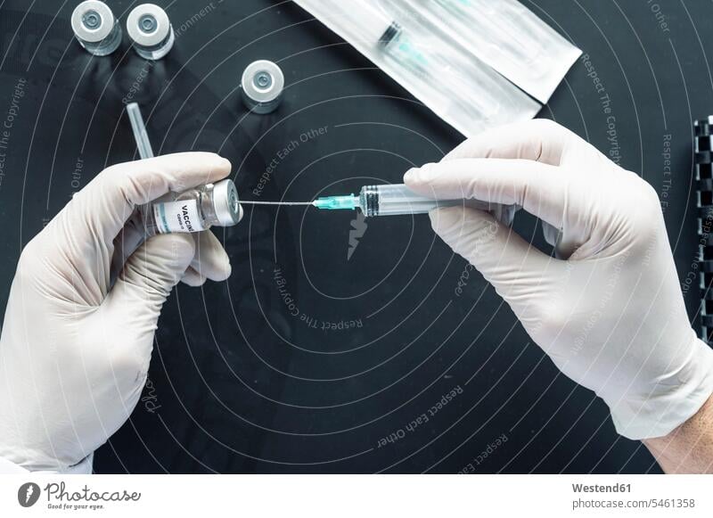 Ausschnitt aus der Hand des Arztes bei der Injektionsspritze in die Impfampulle über Laptop am Labortisch Farbaufnahme Farbe Farbfoto Farbphoto Innenaufnahme