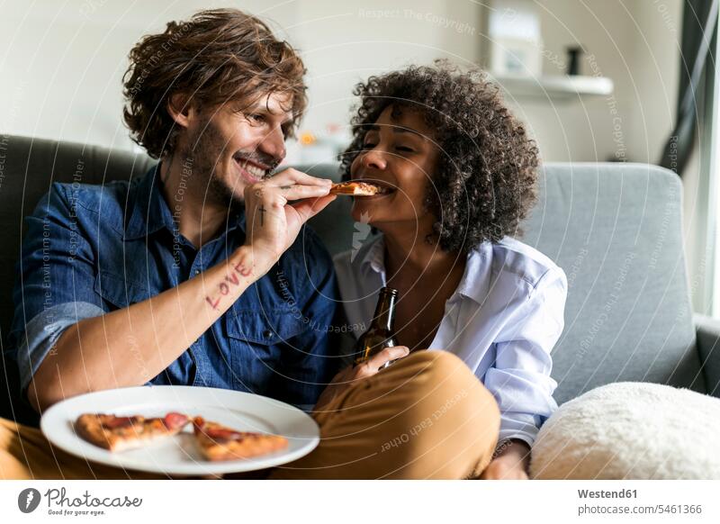 Glückliches Paar sitzt auf der Couch und isst Pizza Pizzen essen essend glücklich glücklich sein glücklichsein Pärchen Paare Partnerschaft sitzen sitzend Sofa