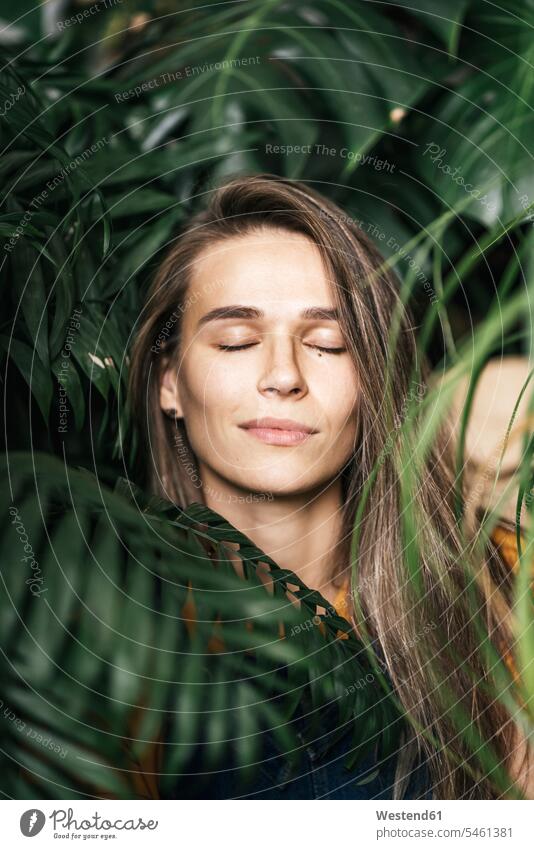 Porträt einer jungen Frau mit geschlossenen Augen inmitten grüner Pflanzen Leute Menschen People Person Personen Europäisch Kaukasier kaukasisch 1 Ein