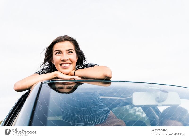Lächelnde junge Frau schaut aus dem Schiebedach eines Autos Wagen PKWs Automobil Schiebedaecher Schiebedächer weiblich Frauen schauen sehend lächeln