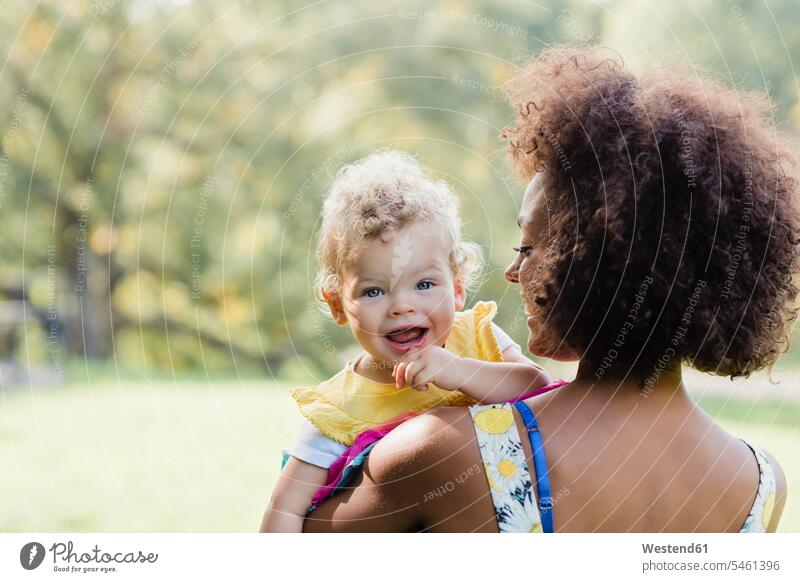 Mutter trägt ein lächelndes Baby, während sie im Park steht Farbaufnahme Farbe Farbfoto Farbphoto Außenaufnahme außen draußen im Freien Tag Tageslichtaufnahme