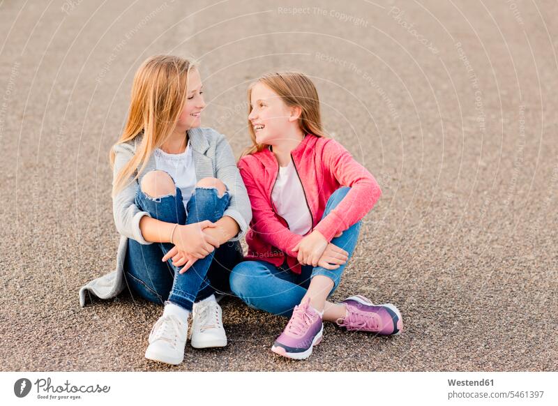 Zwei lächelnde Mädchen sitzen nebeneinander auf dem Boden weiblich Seite an Seite sitzend sitzt Kind Kinder Kids Mensch Menschen Leute People Personen