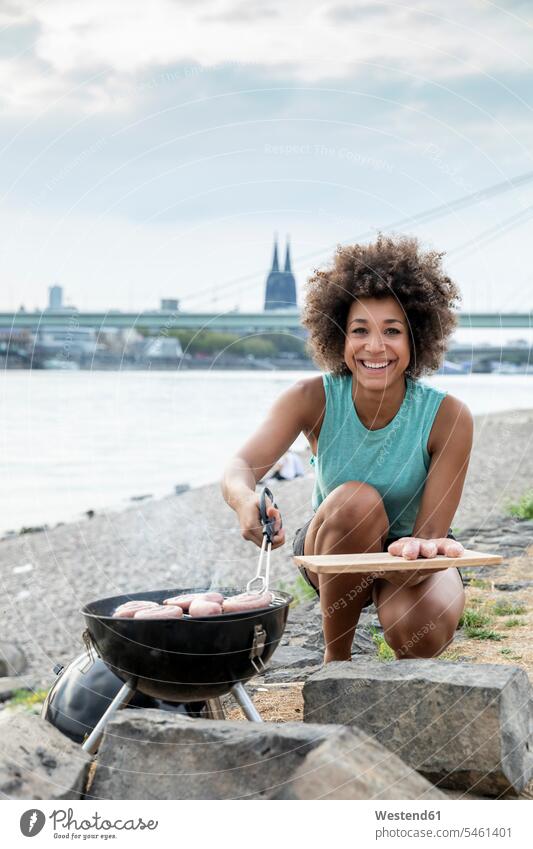 Deutschland, Köln, Porträt einer lächelnden Frau beim Grillen am Flussufer Portrait Porträts Portraits Barbecue Grillparties Grillfest Grillfeste Grillparty