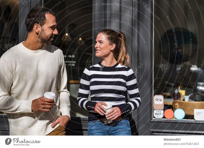 Mann und Frau halten Tassen zum Mitnehmen vor einem Cafe in der Hand und unterhalten sich sprechen reden Kaffee Wegwerfbecher Becher Paar Pärchen Paare